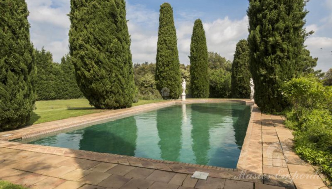Vista de la piscina de la masía rodeada de cipreses 