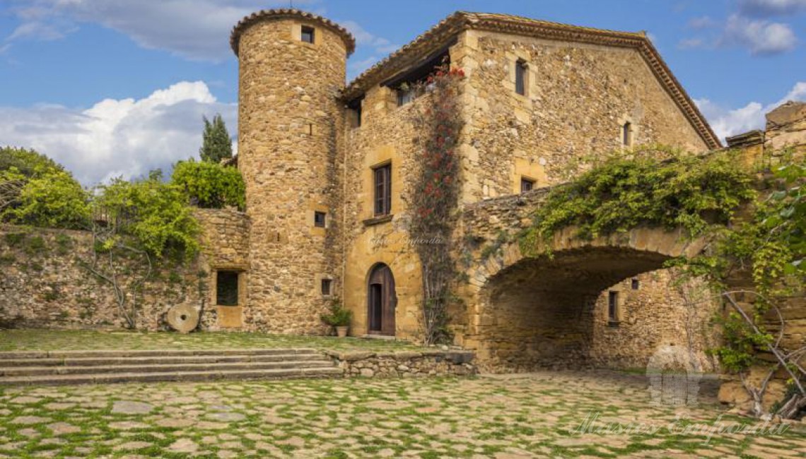 Vista del interior del patio que parece de la entrada a la masía con torre circular de defensa y puente arcado de piedra que soporta terrada con espectaculares vistas a los campos de la propiedad 