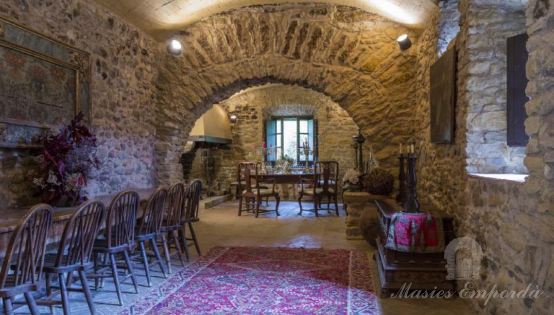 Vista general del amplio comedor principal de la casa con arco en piedra y la chimenea al fondo del salón 
