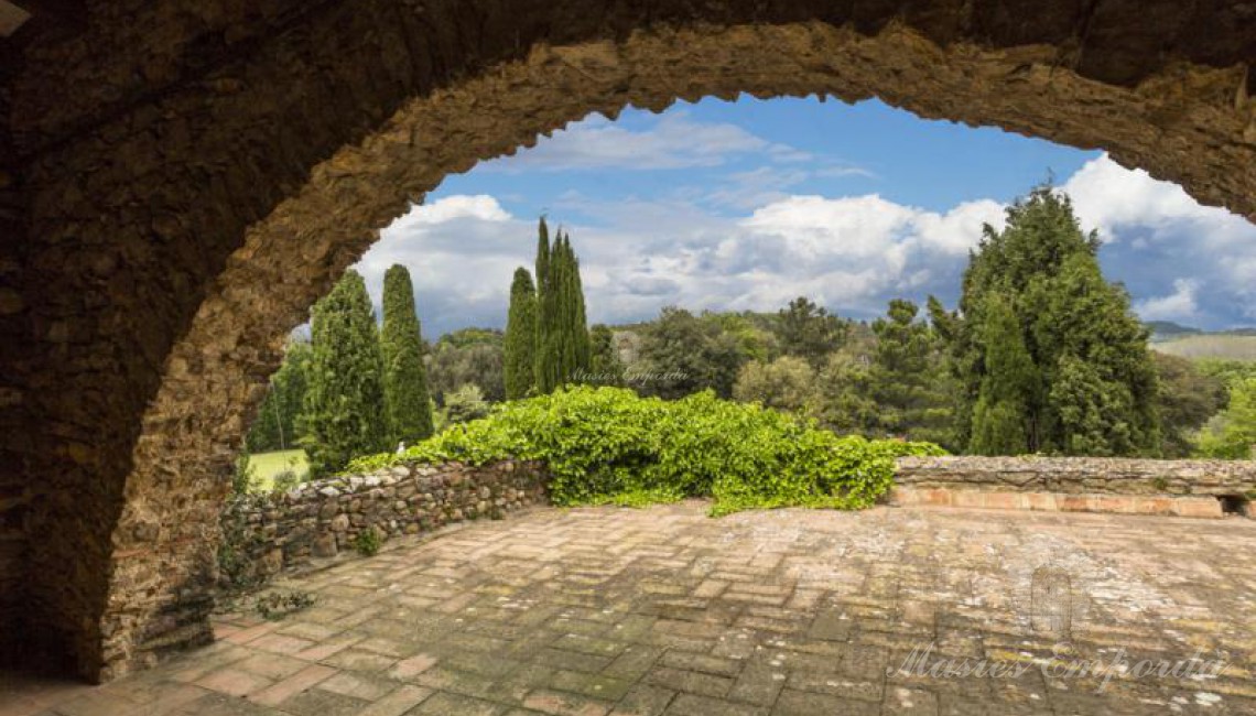 Detalle de la terraza y del arco de piedra de esta con vistas al jardín y los campos de la propiedad
