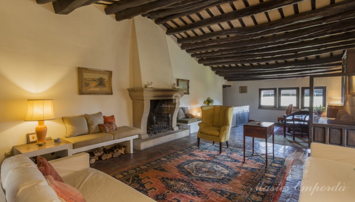 Salón principal de la masía con chimenea y salida a la terraza cubierta con vistas únicas de la comarca