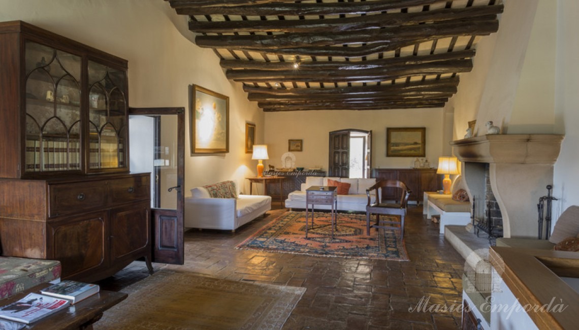 Desde otro ángulo salón principal de la masía con chimenea y salida a la terraza cubierta con vistas únicas de la comarca