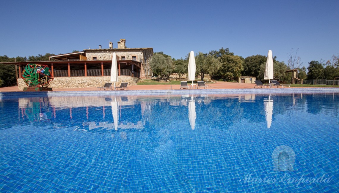 Vistas de la zona de piscina con la masía la fondo de la imagen 