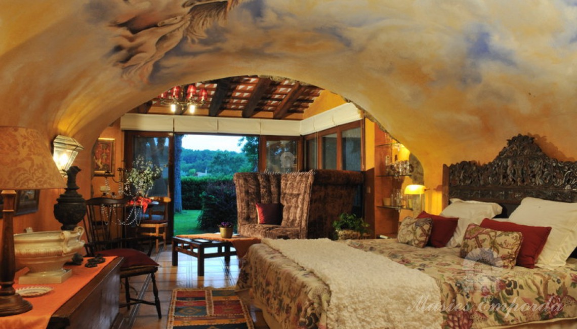 Detalle de la habitación con parte de la cubierta abovedada con frescos pintados en ella y el salón al fondo de la imagen con vistas al jardín, simplemente espectacular. 