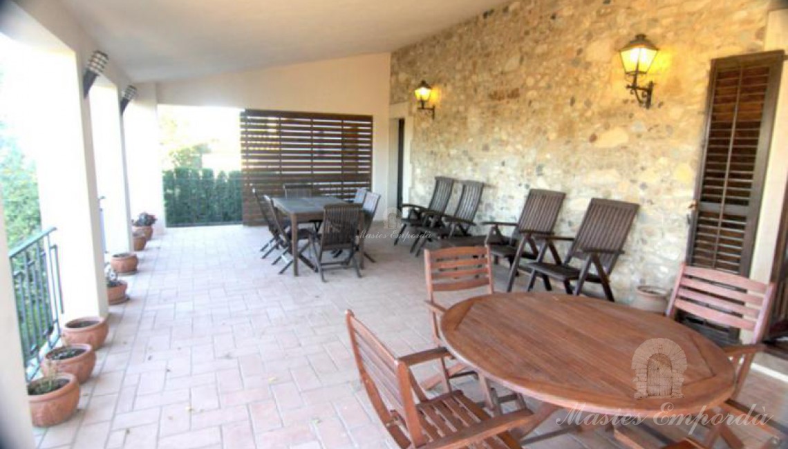 Porche bajo terraza de planta con mesas de madera y vista al jardín y a la piscina 