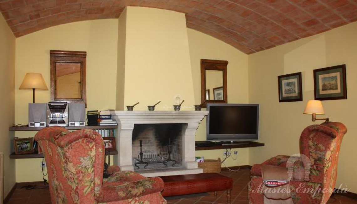 Salón de estar abovedado con la chimenea en el centro don dos sillones orejeros 