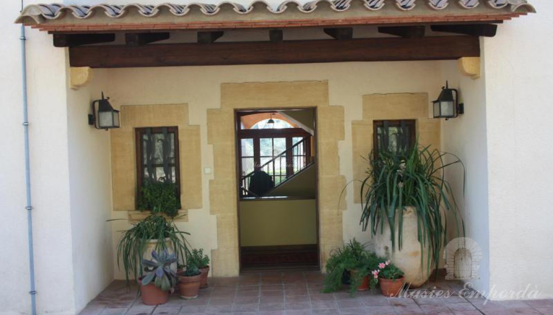 Entrada posterior de la casa con puertas y ventana con dinteles y pilares en piedra con pequeño porche cubierto de teja con vigas de madera 