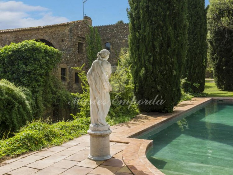  Vista de la piscina rodeada de cipreses con una preciosa estatua estilo romano y como fondo la masía  