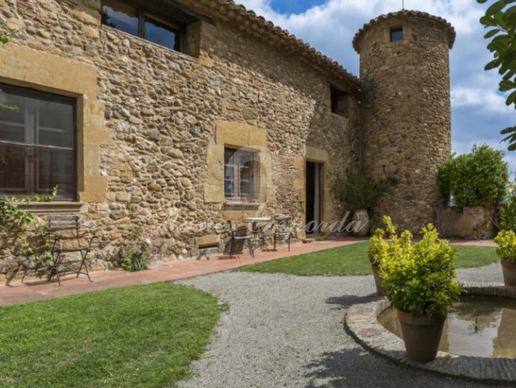 Vista del interior del patio superior de la casa con entrada lateral a la masía con torre circular de defensa y jardín con pequeño estanque. 