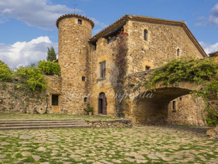 Vista del interior del patio que parece de la entrada a la masía con torre circular de defensa y puente arcado de piedra que soporta terrada con espectaculares vistas a los campos de la propiedad 