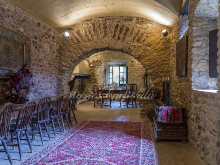Vista general del amplio comedor principal de la casa con arco en piedra y la chimenea al fondo del salón 