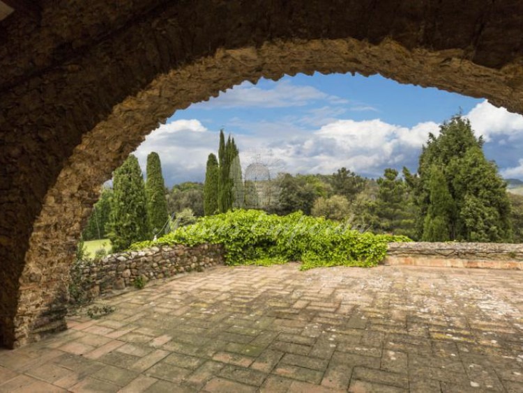 Detalle de la terraza y del arco de piedra de esta con vistas al jardín y los campos de la propiedad