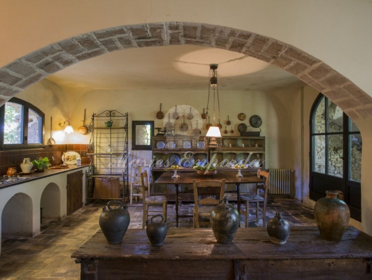 Detall de la cuina menjador de la casa de convidats de la propietat adjunta a la masia principal amb arc de pedra de càrrega s de la segona planta.