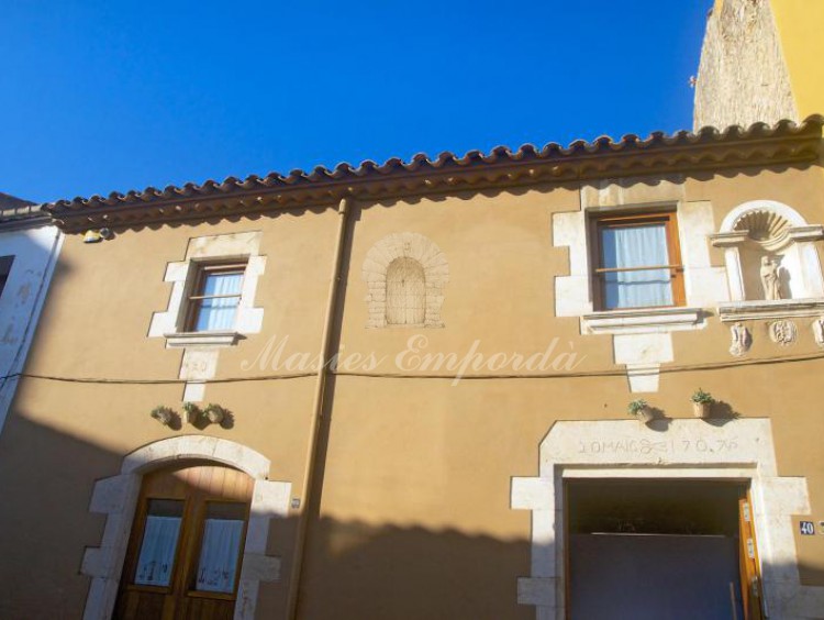 Facha de esta preciosa casa en venta en Palafrugell, con el dintel de la puerta y los pilares en piedra pulida blanca que resalta con el marro claro de la fachada de la casa